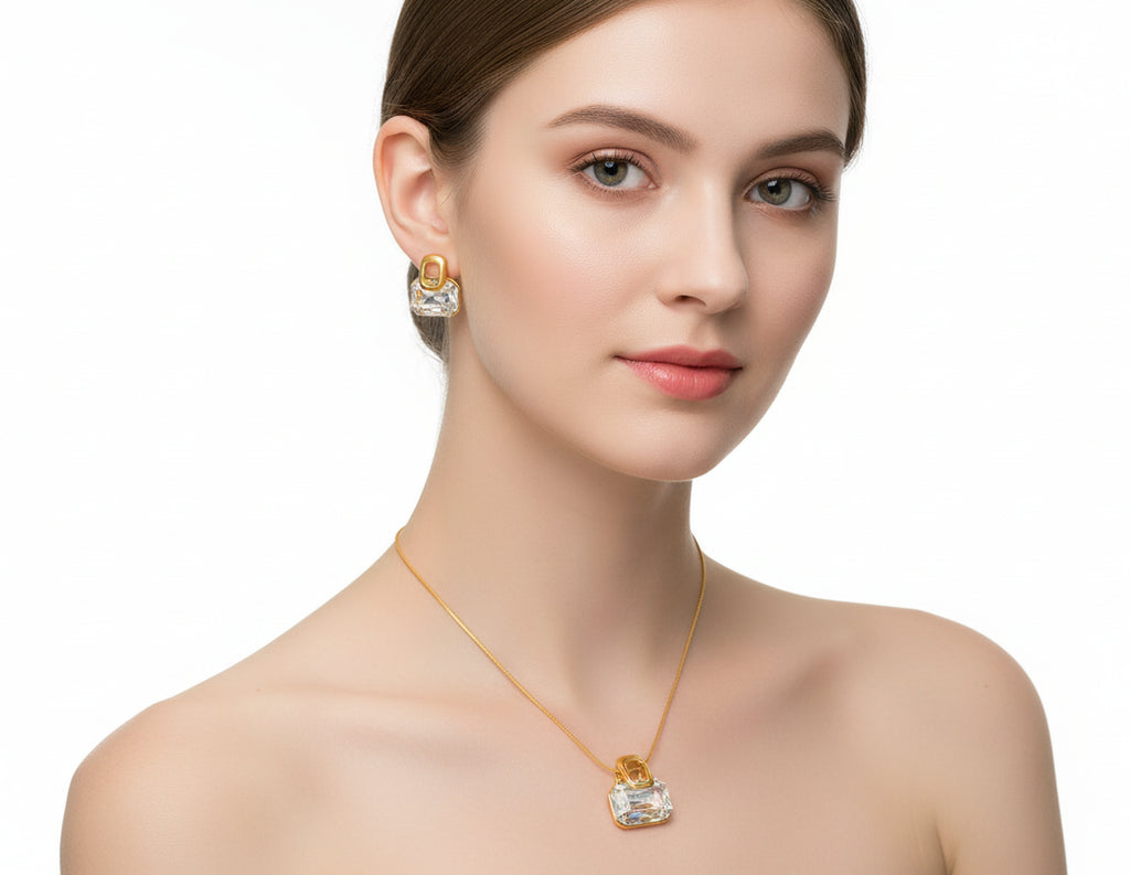 Gold necklace and earrings with clear gemstones on a gray surface