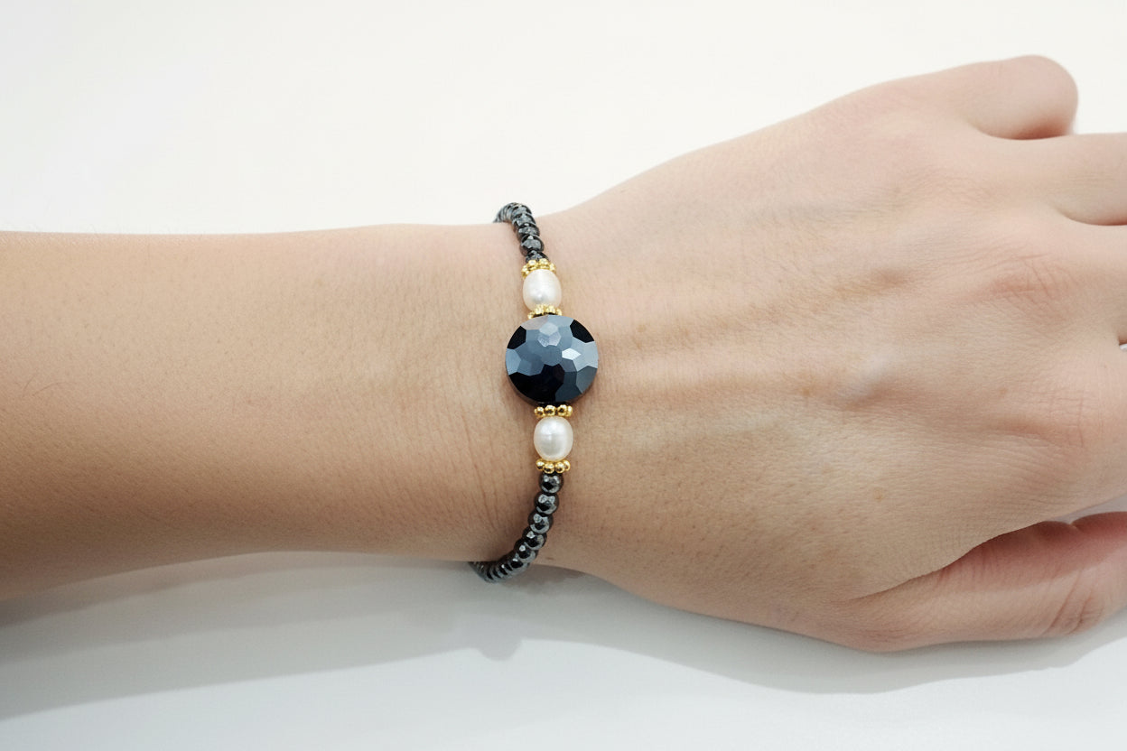 Bracelet with black beads and a large central stone on a wrist against a white background