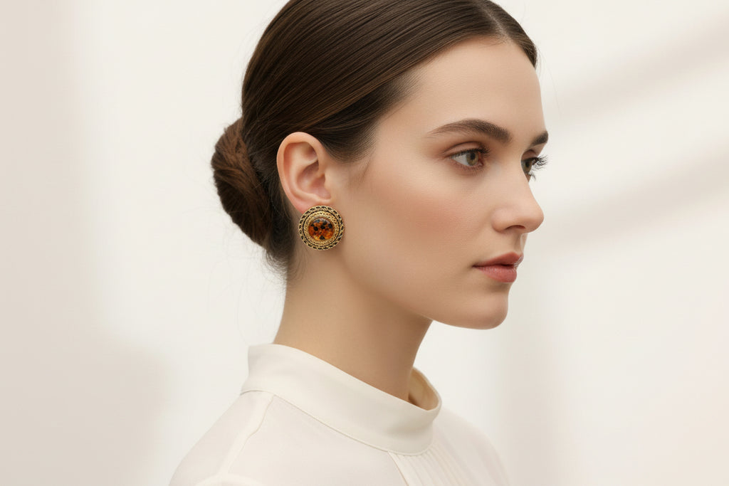 Pair of round earrings with gold and black-brown design on a white stand