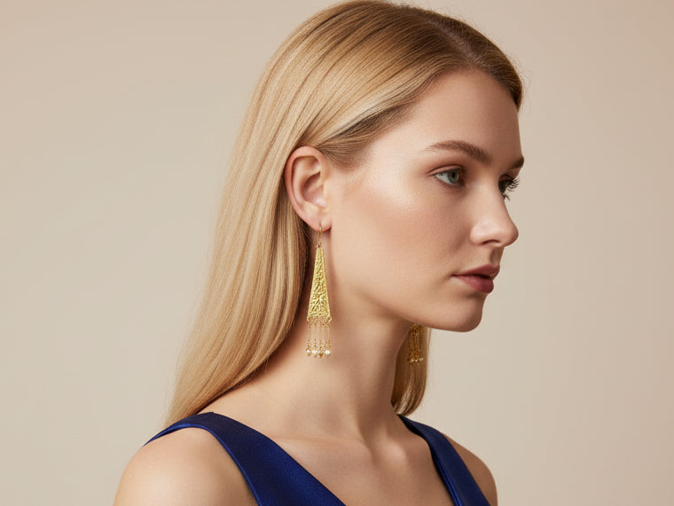 Close-up of a person wearing gold tassel earrings with studio background.