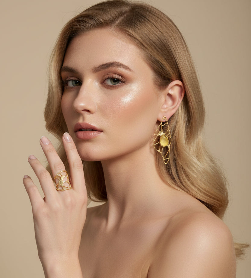 Close-up of a person wearing gold earrings and a matching ring, with a studio backround background.