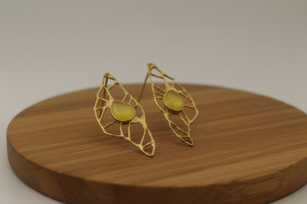 Gold earrings with yellow gemstones on a wooden surface.