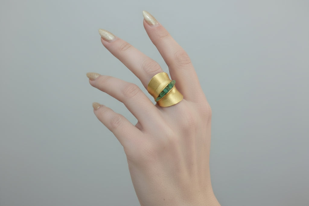 Gold ring with green gemstones on a finger against a neutral background