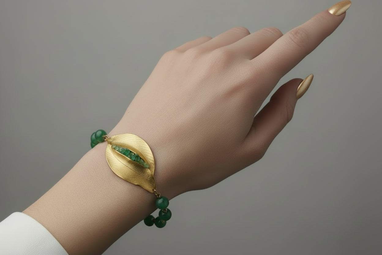 Hand wearing a green and gold bracelet on a studio background