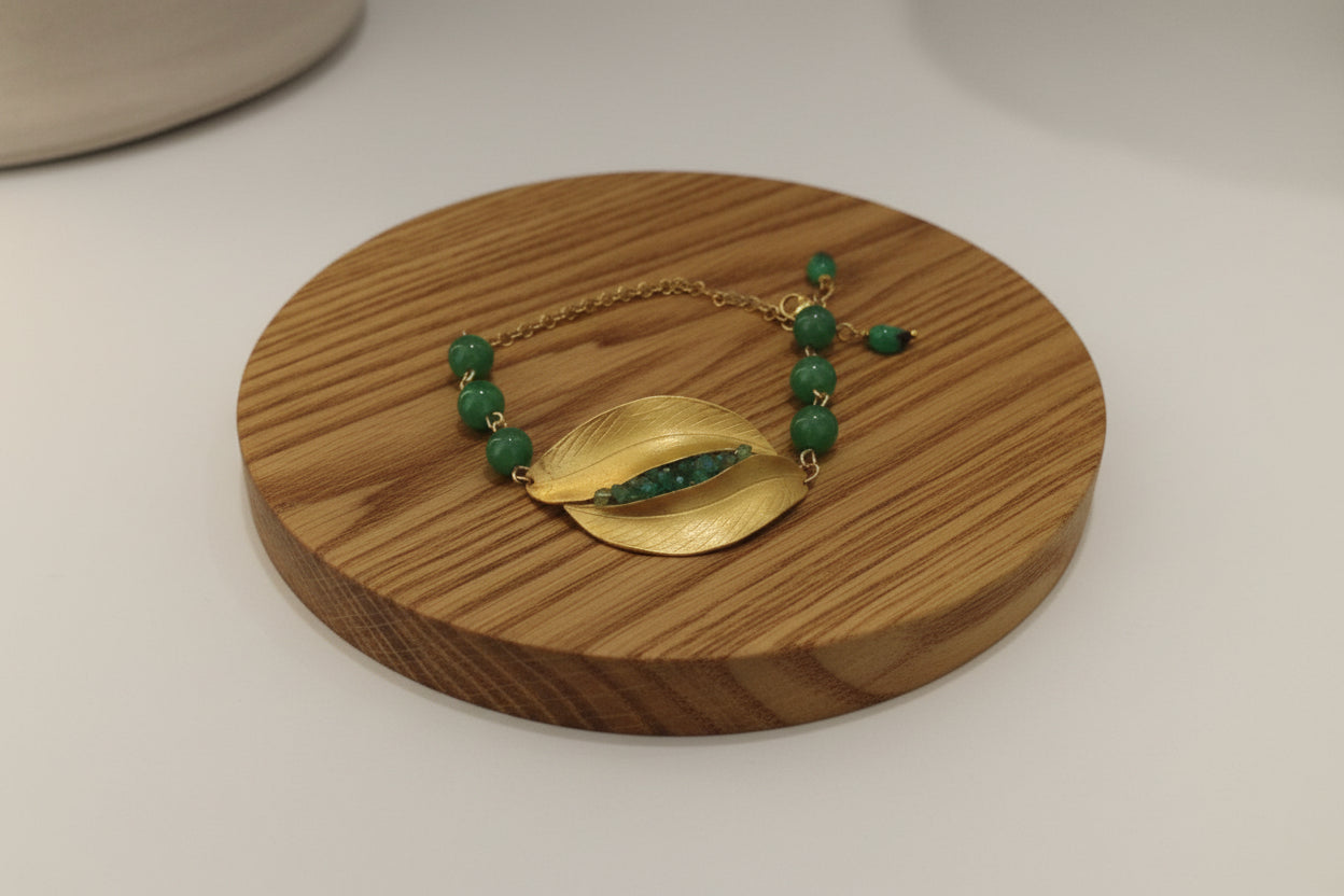 Gold bracelet with green beads on a wooden surface.