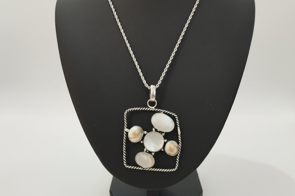 Silver necklace with a square pendant featuring circular stones on a black stand.