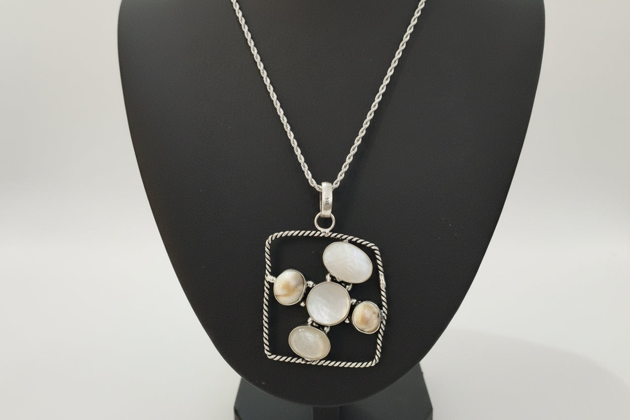 Silver necklace with a square pendant featuring circular stones on a black stand.
