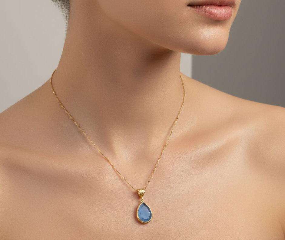 A woman is wearing a necklace with gold thin chain and a pendant with blue stone 