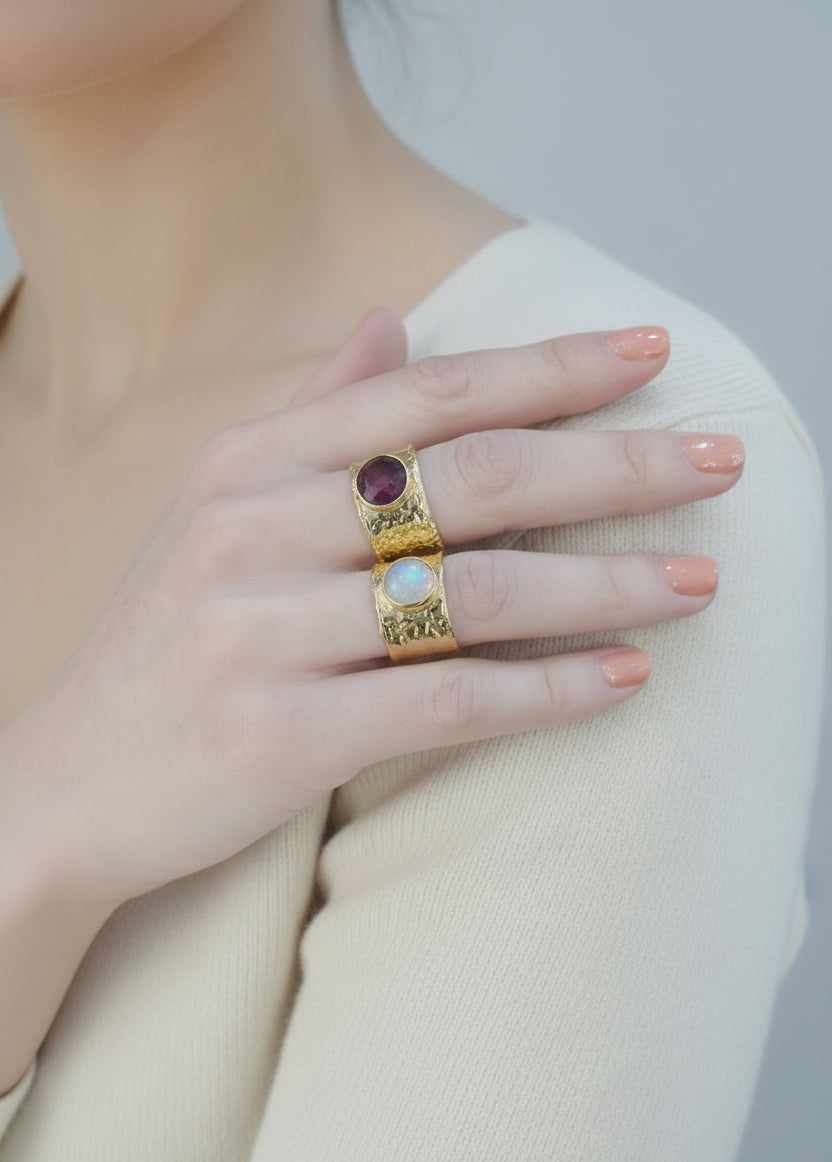 Gold rings with gemstones on a person's finger against a dark background