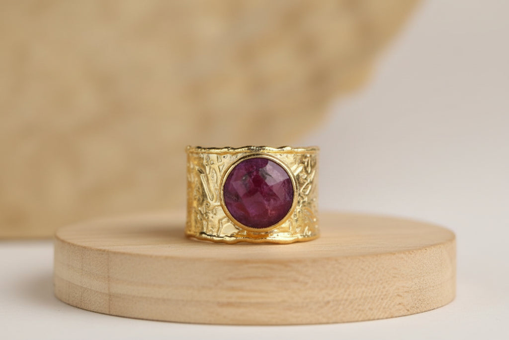A gold ring with red gemstone on a wooden surface