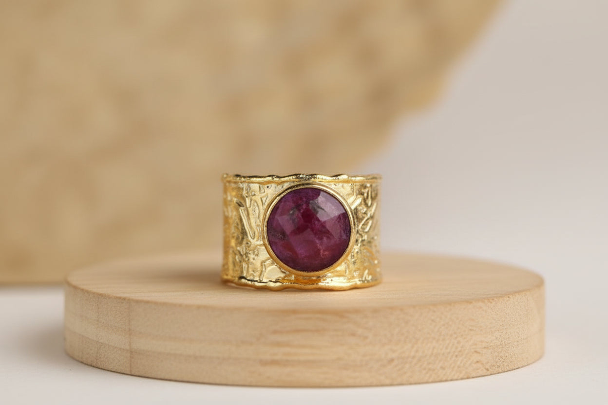 A gold ring with red gemstone on a wooden surface